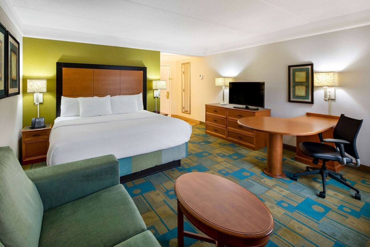 Ein Hotelzimmer mit einem Bett, einem Schreibtisch, einem Stuhl, einem Fernseher und einem kleinen Tisch.