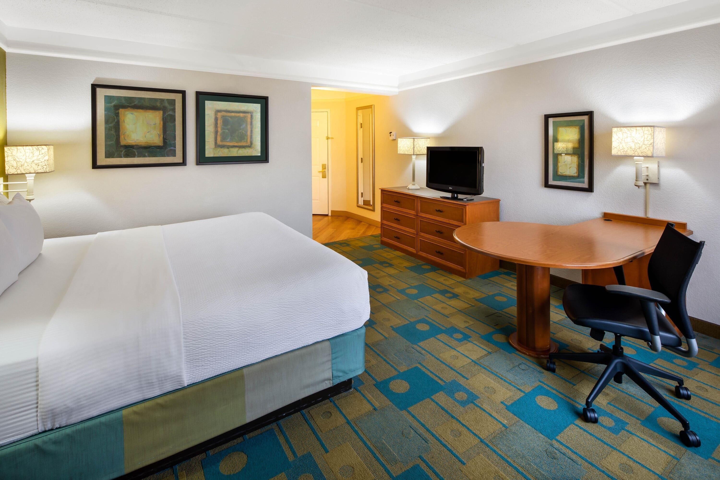 A hotel room with a bed, a desk, a chair, a television, and two wall-mounted lamps.