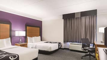 Quarto de hotel com duas camas, uma escrivaninha, uma cadeira, janela com cortinas e ar condicionado fixado na parede.