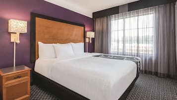 A hotel room with a large bed, two bedside tables, a wooden headboard, and a window with sheer curtains.
