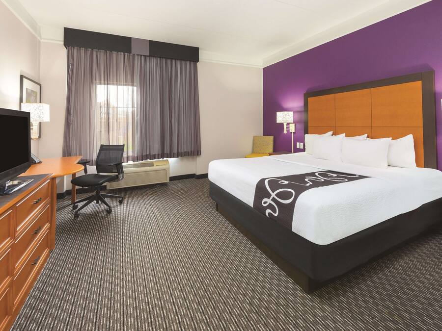 Une chambre d’hôtel avec un grand lit, un bureau avec un ordinateur, une télévision et une chaise.