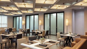 Un'area ristorazione di un hotel moderna, con diversi tavoli e sedie, ampie finestre e lampade dal design contemporaneo.