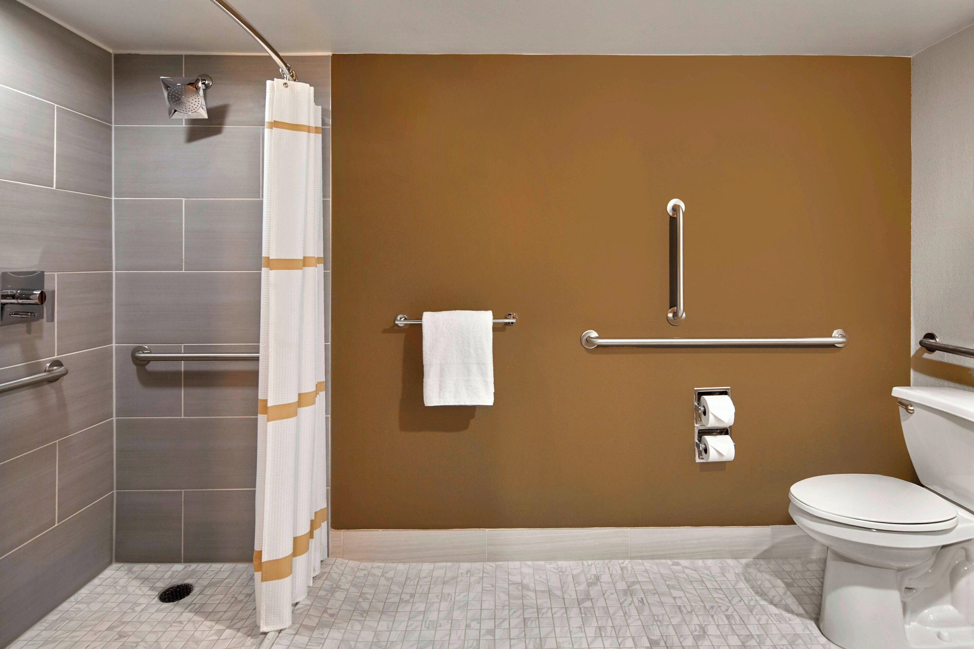 A bathroom with a shower, grab bars, a toilet, and a towel rack.