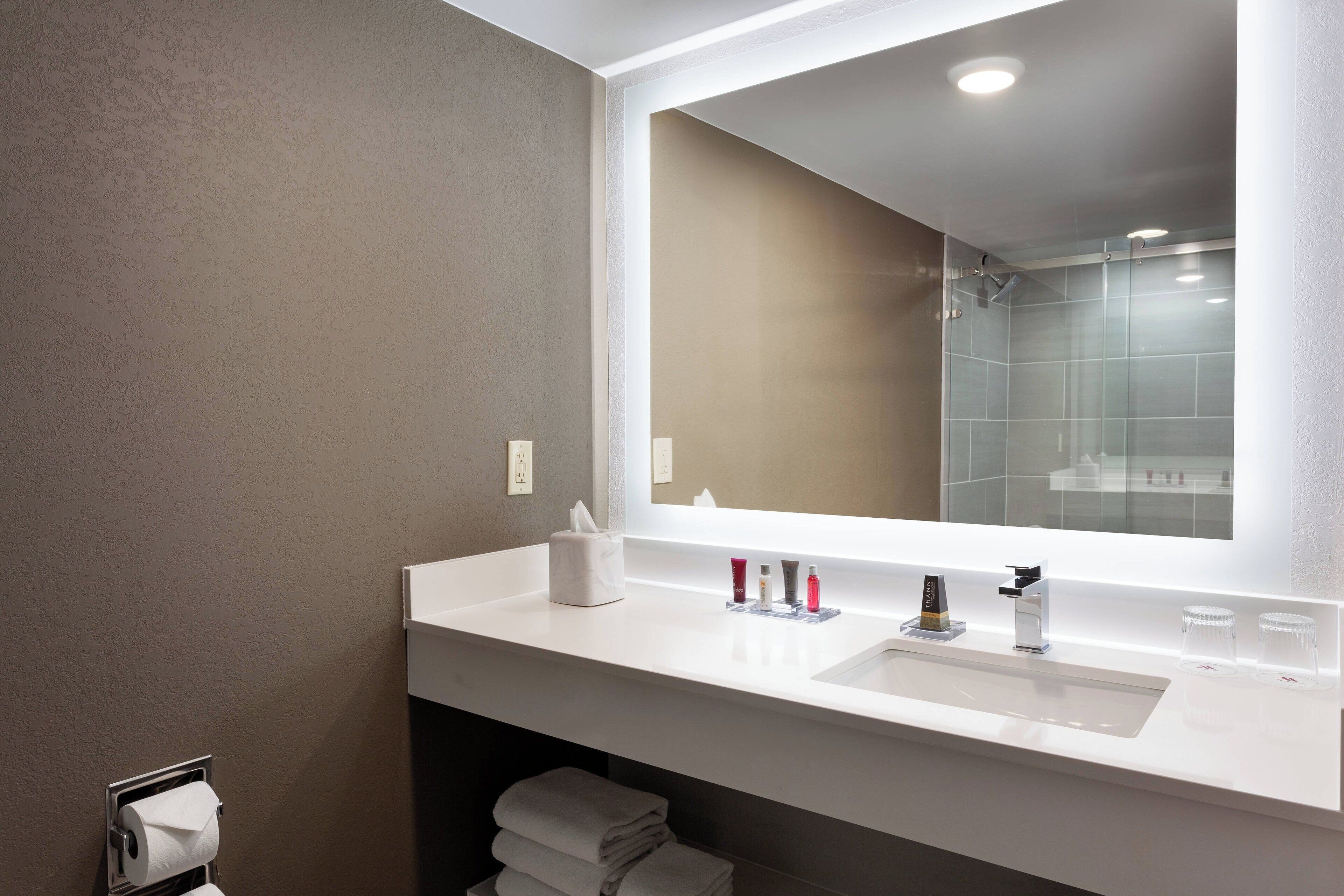 A modern bathroom with a large mirror, white sink, and a glass shower enclosure.