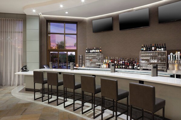 Un área de bar moderna con una barra larga, taburetes y una exhibición de vinos y licores.