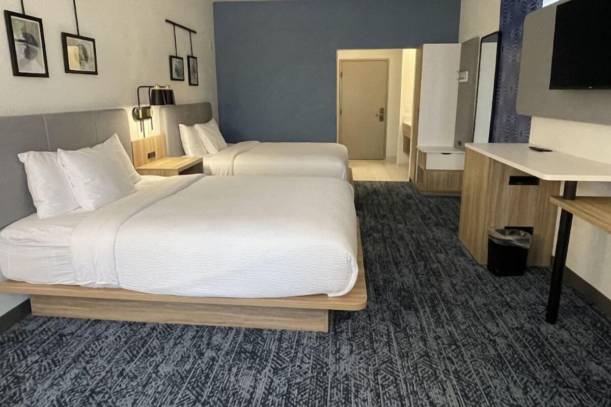 A hotel room with two beds, a desk, a TV, and a door leading to a bathroom.