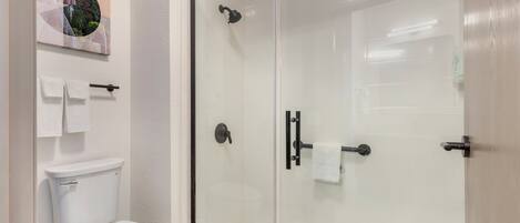 A modern bathroom with a glass-enclosed shower, a white toilet, and a wall-mounted towel rack.