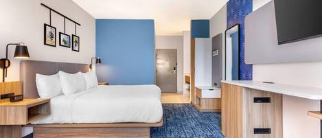 A modern hotel room with a bed, bedside tables, a desk, a flat-screen TV, and a bathroom with a mirror and sink.
