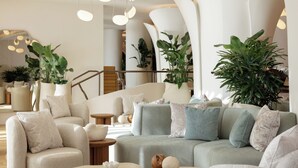Un salon moderne avec un canapé d’angle, des tables basses rondes et de nombreuses plantes en pot.