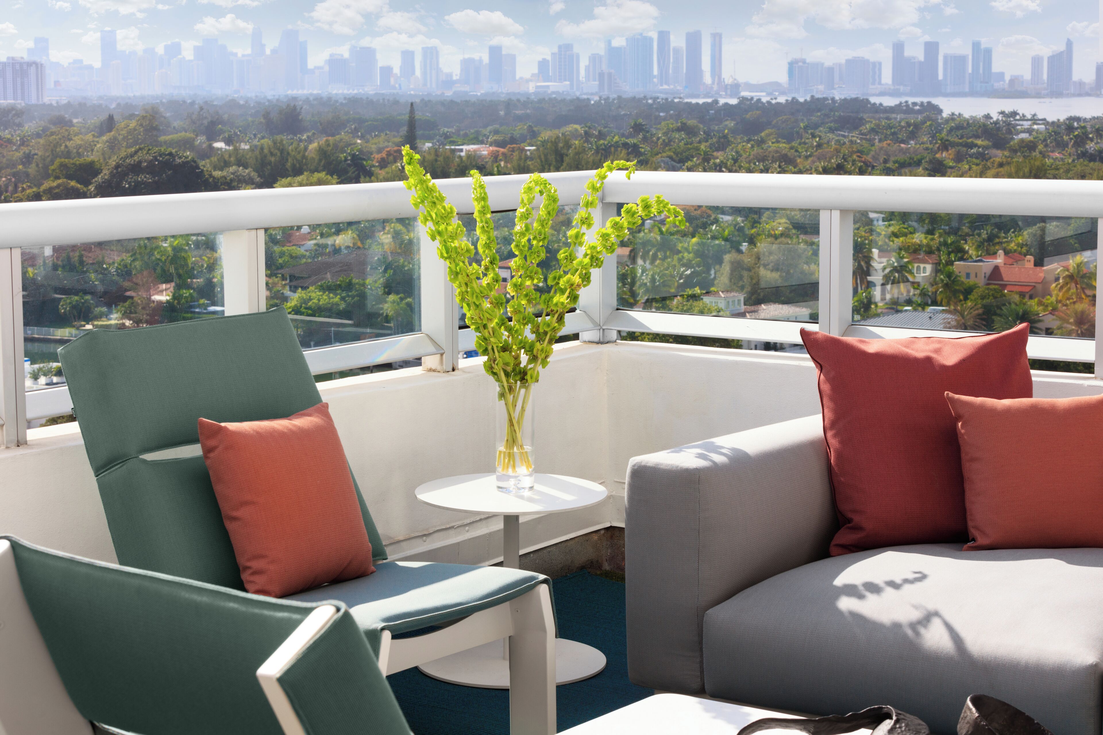 Un balcon offrant une vue sur les toits de la ville, avec des sièges verts et gris et un vase contenant des plantes vertes.