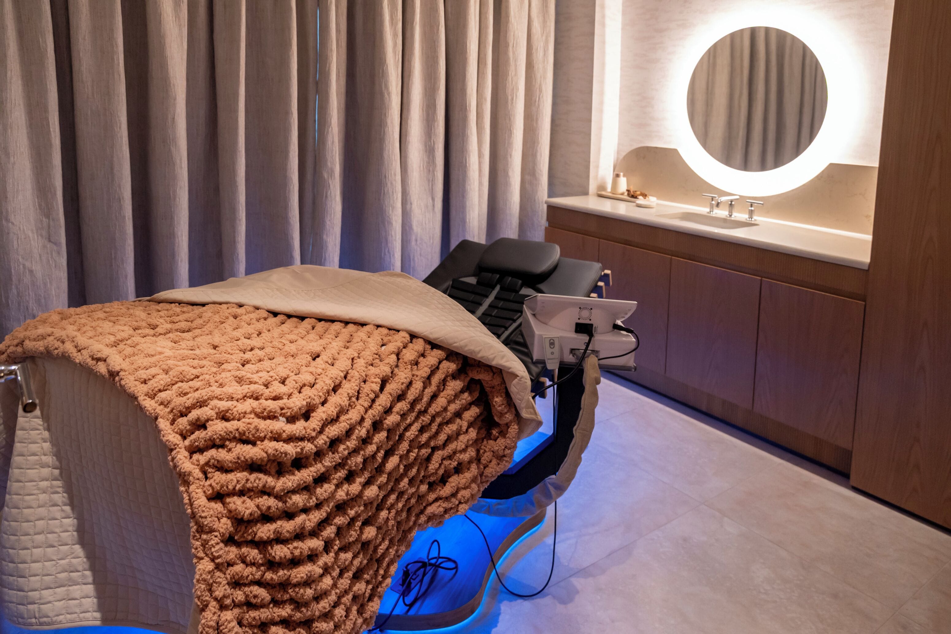 A room with a massage chair, a large mirror, and a wooden cabinet.