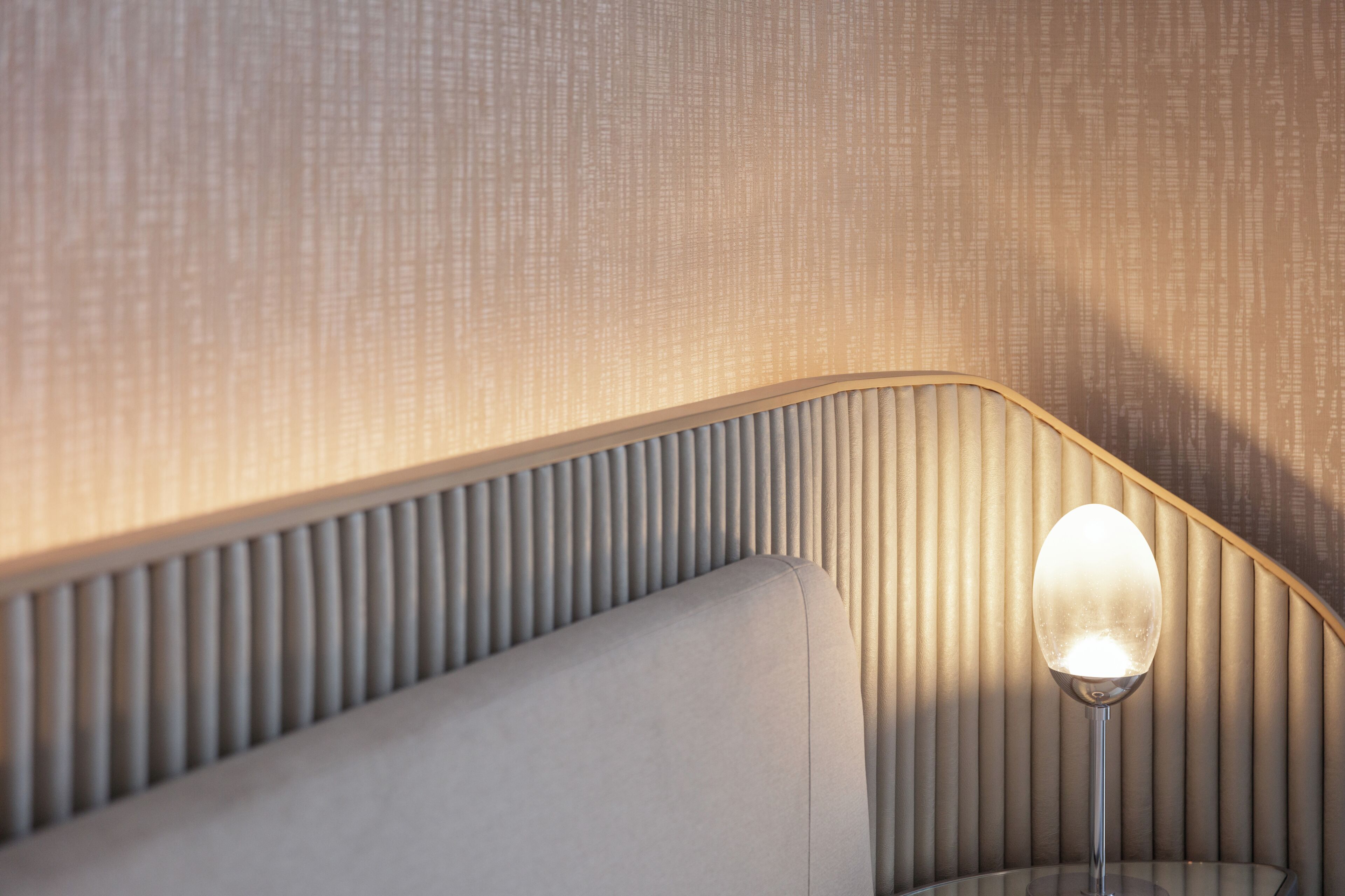 A corner of a room with a textured wall, a curved bench, and a lamp with a clear glass shade.