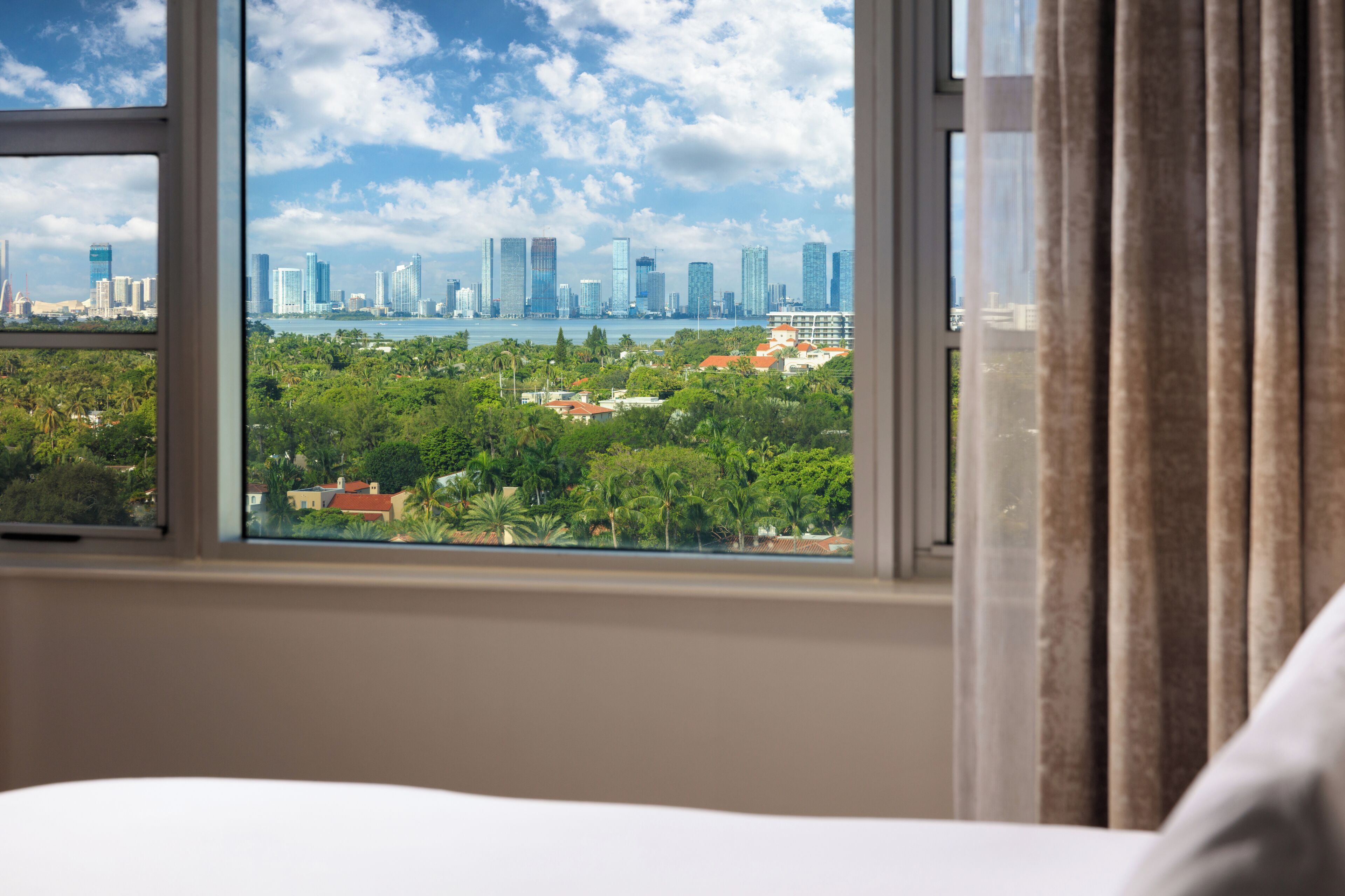 Ein Hotelzimmer mit großem Fenster und Blick auf Skyline und Grünflächen.