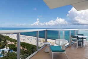 Un balcon avec vue sur une plage, une piscine et une table avec des chaises.