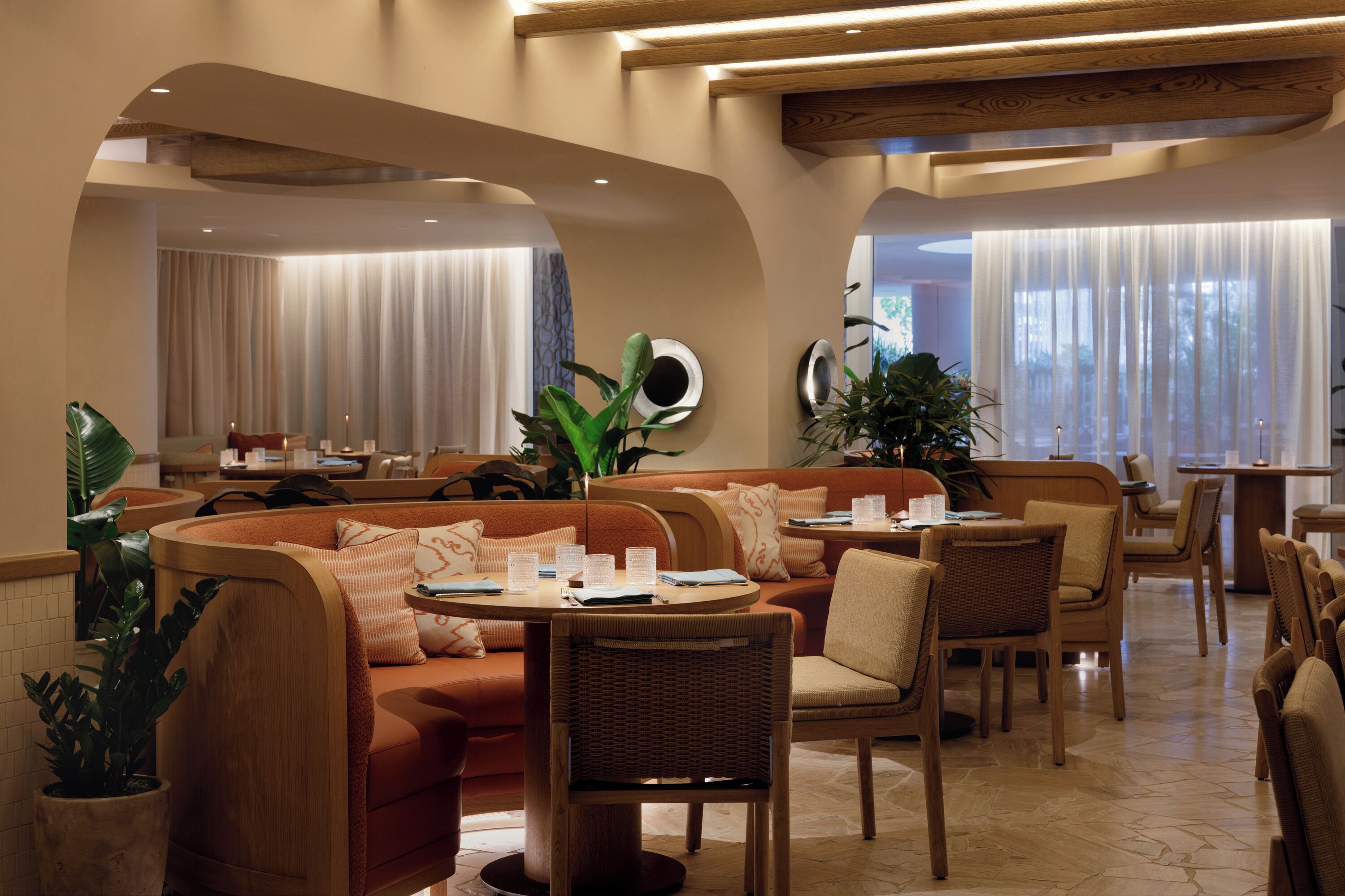 Un vestíbul d'hotel modern amb zones d'estar, taules i plantes en testos.