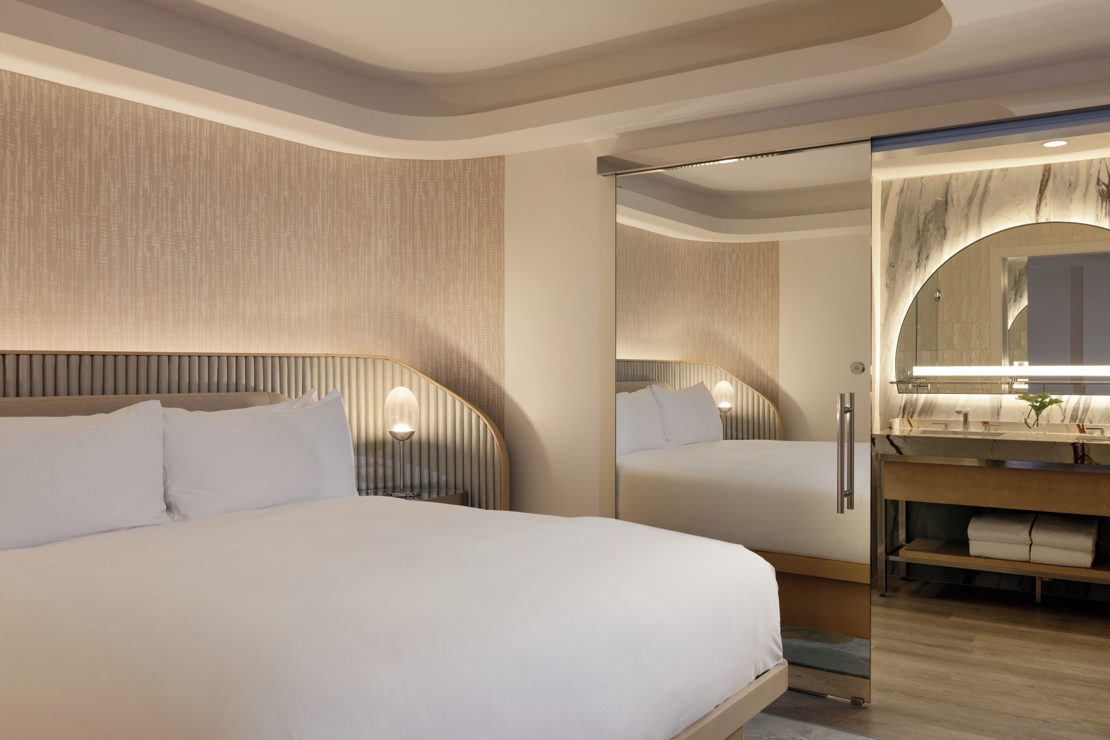 Ein modernes Hotelzimmer mit einem großen Bett, einem Badezimmer mit Waschtisch und einem Spiegel.