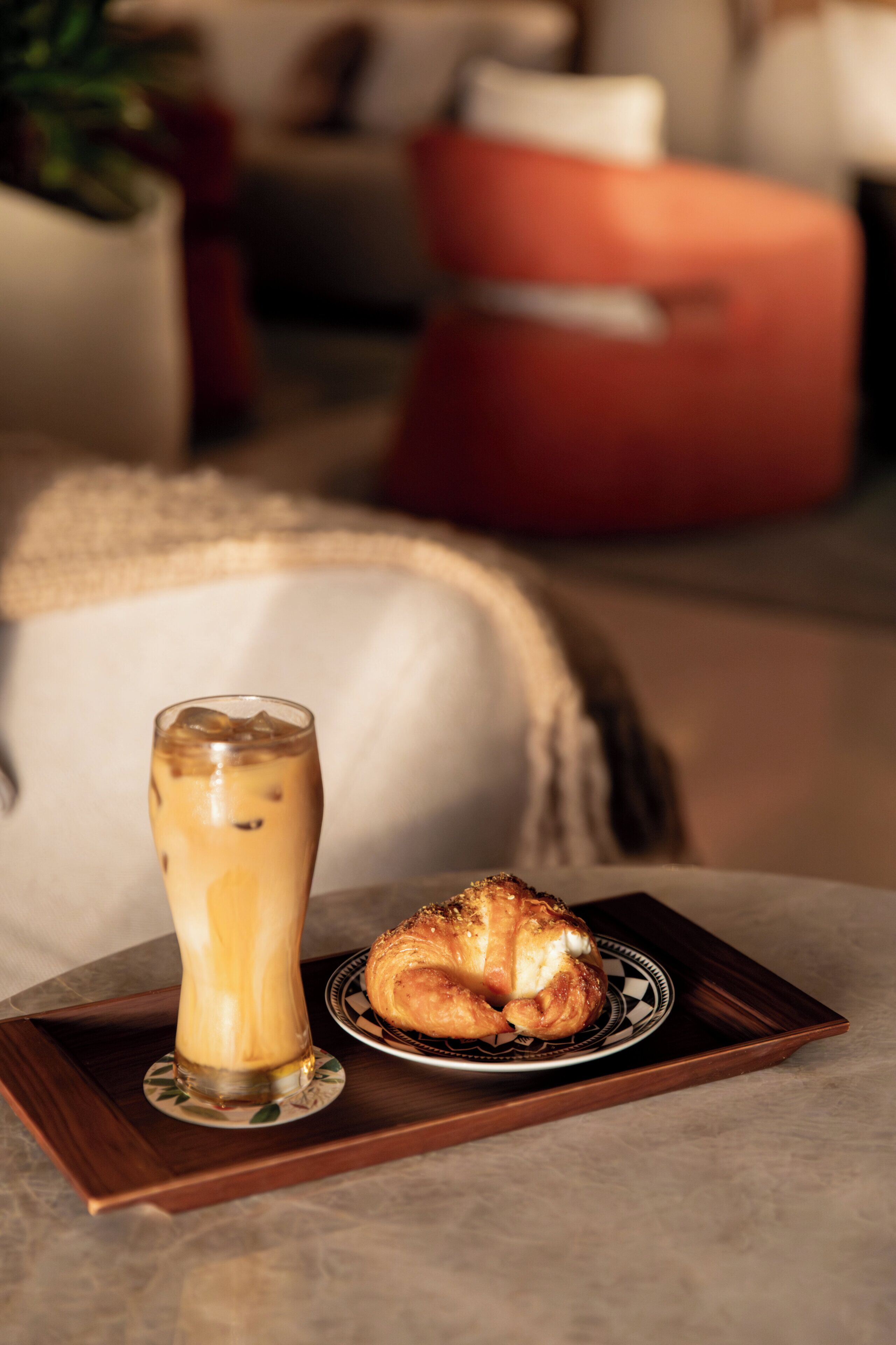 Ein Tablett mit einem Glas Eistee und einem Croissant auf einem Tisch in einer gemütlichen Innenraumgestaltung.