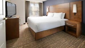 Quarto de hotel com uma cama grande, uma televisão em uma cômoda de madeira e uma mesa de cabeceira com abajur.