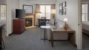 Ein Hotelzimmer mit Flachbildfernseher, einer Couch, einem kleinen Tisch, einem Kamin und einem Fenster mit Vorhängen.