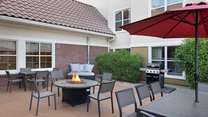 Eine Außenpatio mit einem runden Tisch, Stühlen, einer Feuerstelle und einem Grill.