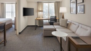 Ein Hotelzimmer mit Bett, Schreibtisch, Sofa, Fernseher und einem Fenster mit Vorhängen.