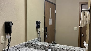 A bathroom with a granite countertop sink, a hairdryer, and a mirror with lights.