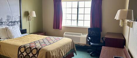 Ein Hotelzimmer mit Bett, Schreibtisch, Stuhl, einem Fenster mit Vorhängen, einer Klimaanlage und einer Wandlampe.