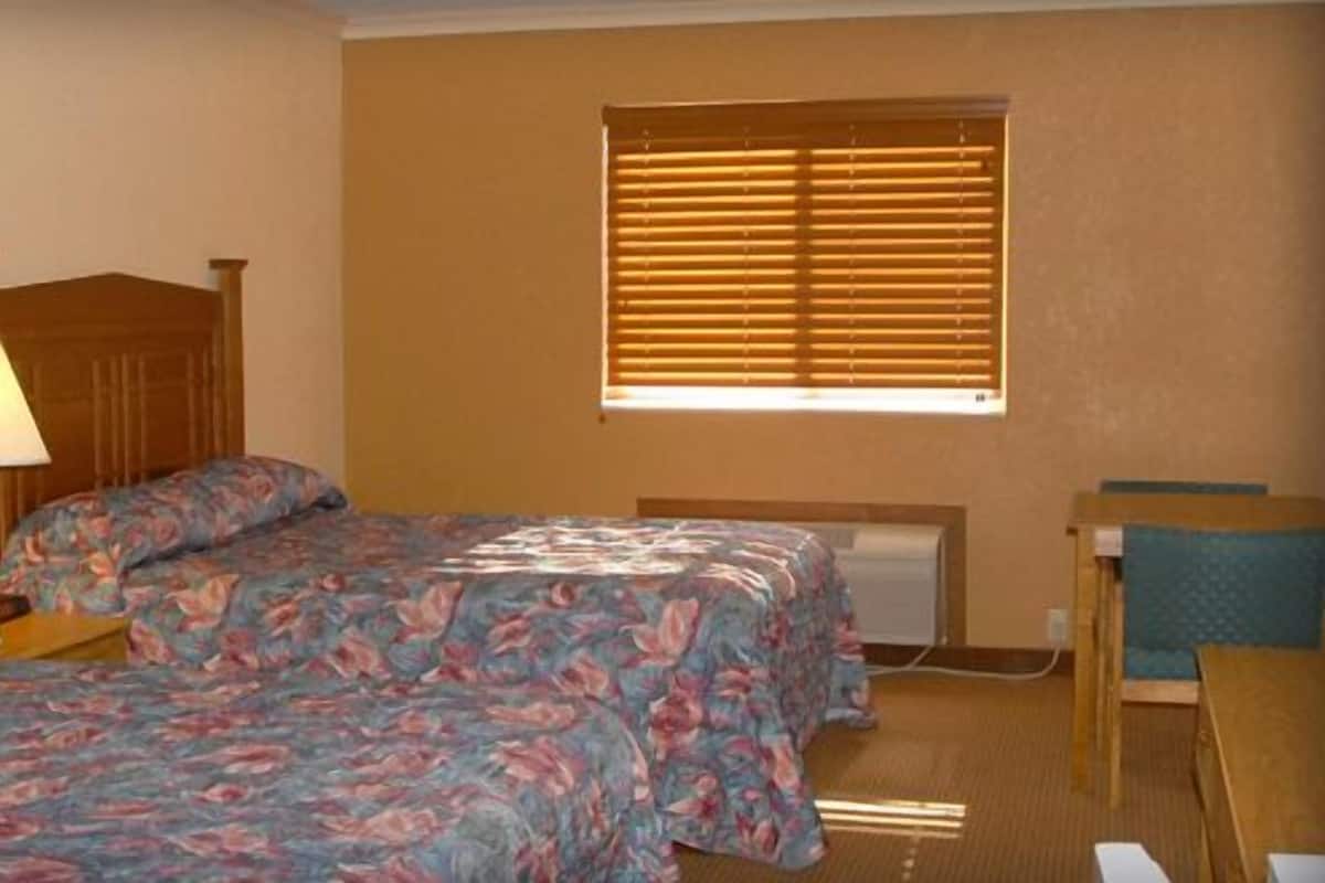 Quarto de hotel com cama, abajur, janela com persianas e uma pequena mesa.