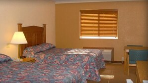A hotel room with a bed, a bedside lamp, a window with blinds, and a small table.