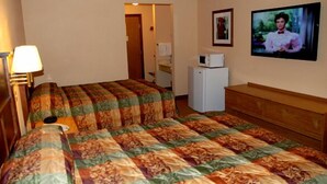 A room with two beds, a wooden dresser, a microwave, and a television on the wall.