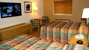 A hotel room with a bed, a desk, a chair, a lamp, and a television on the wall.