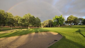 Un campo de golf con un búnker de arena, árboles y un arcoíris.