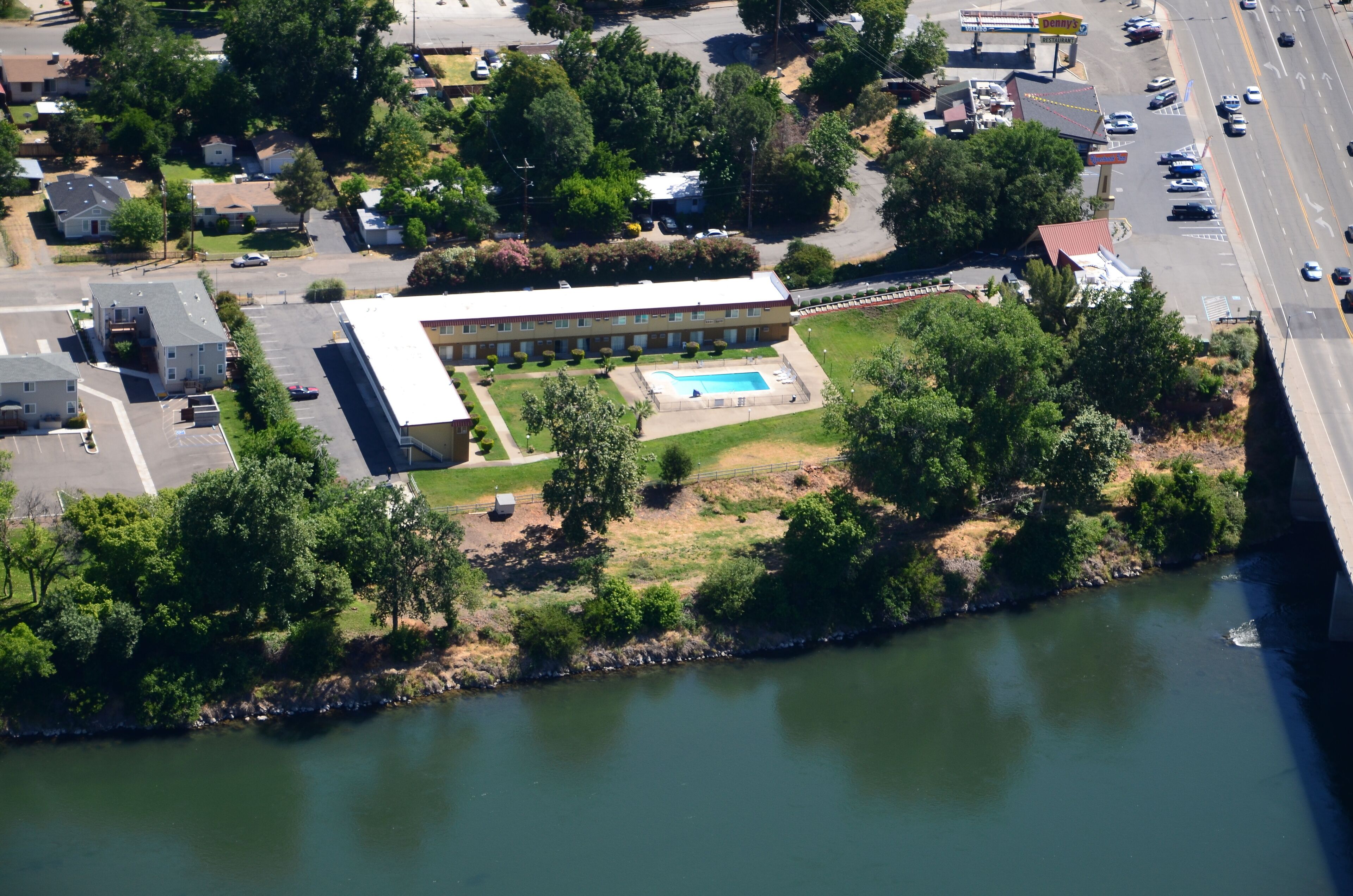 An aerial view of a building with a swimming pool, surrounded by greenery and a river.