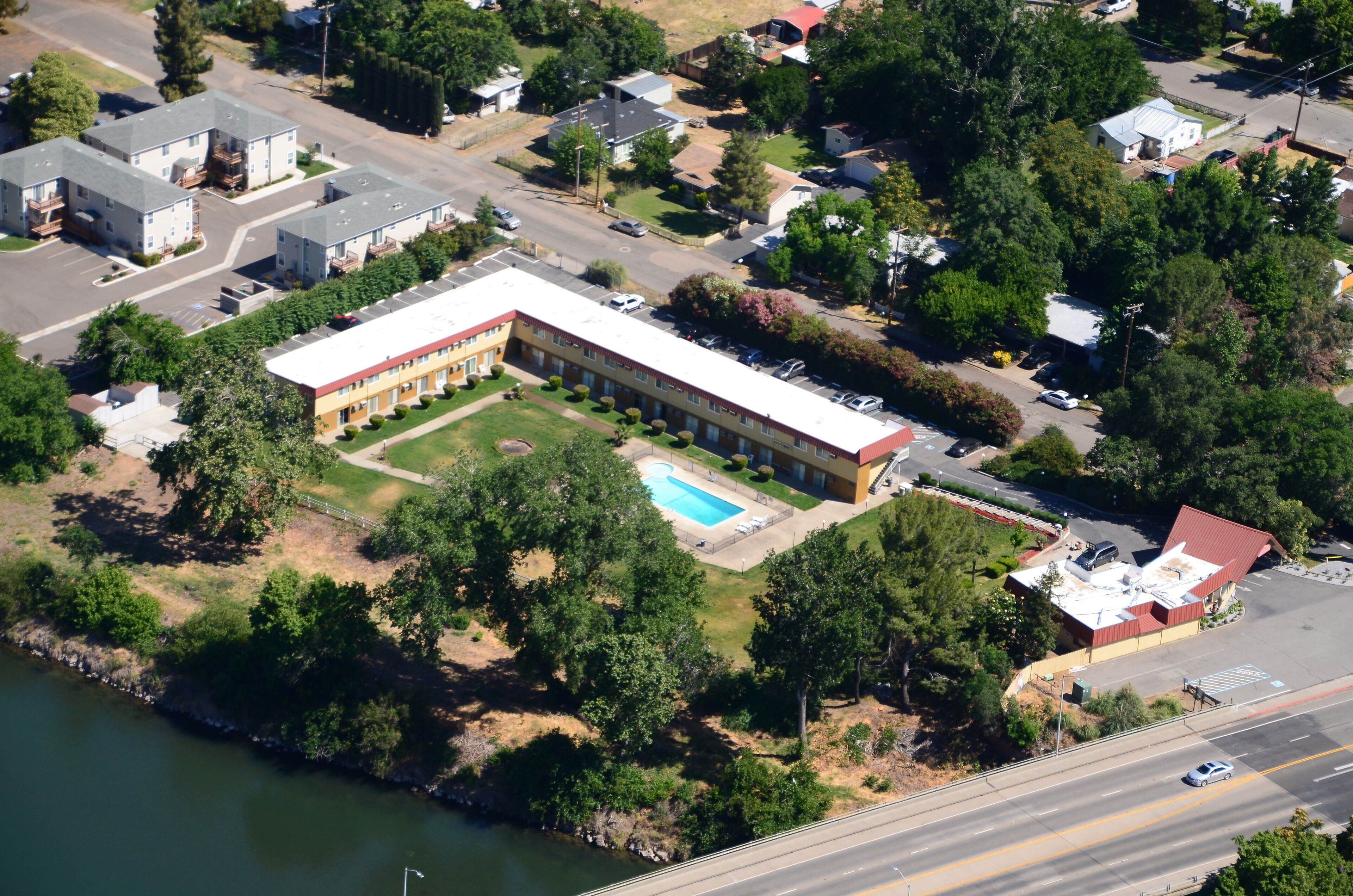An aerial view of a building with a swimming pool, surrounded by greenery and a body of water.