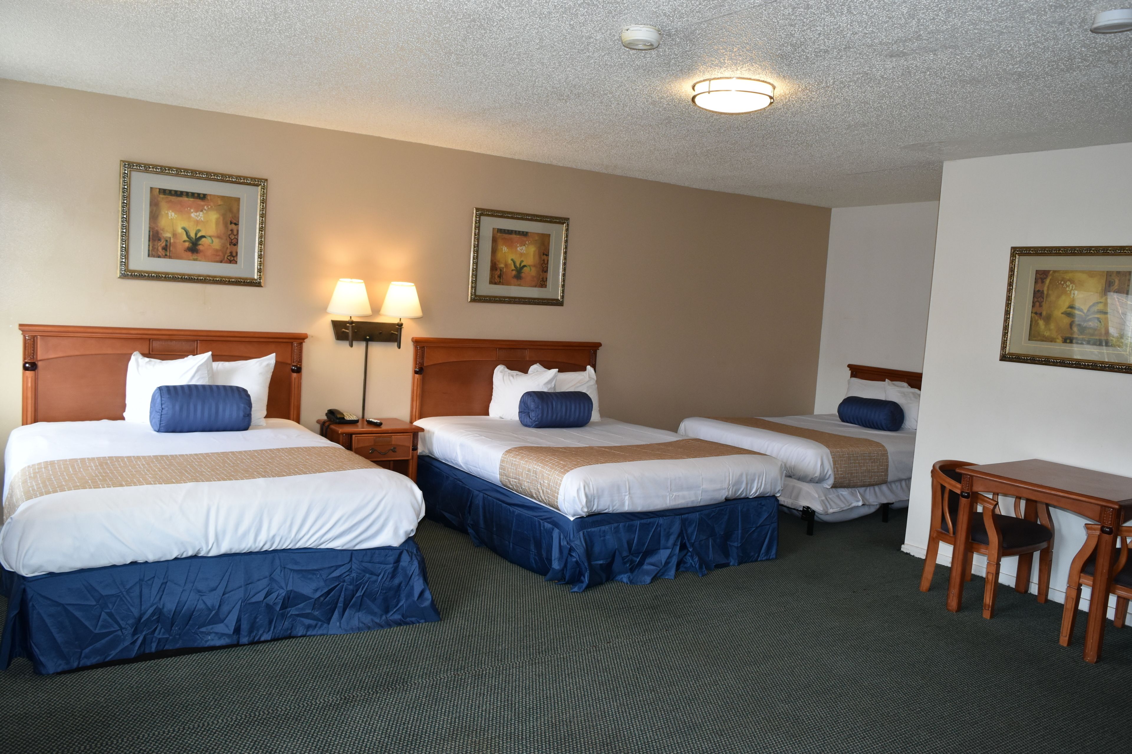 A hotel room with two beds, a desk, and a chair. There are two bedside lamps and a ceiling light.