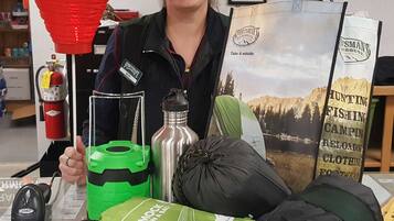 A person holding various outdoor gear items, including a green water bottle, a black bag, and a red lantern.