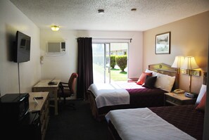 Habitación de hotel con dos camas, un escritorio con silla, televisor y ventana con cortinas.