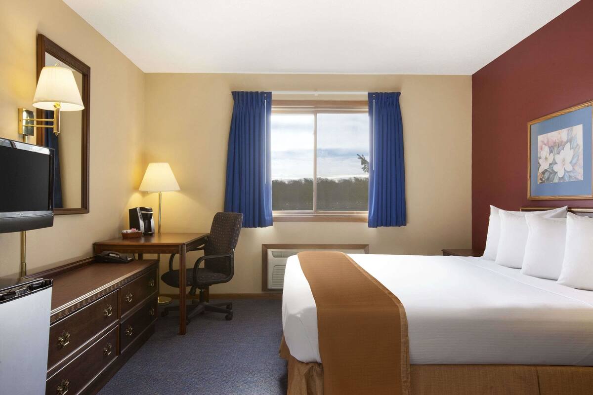 A hotel room with a bed, a desk with a lamp, a chair, a dresser, and a TV.