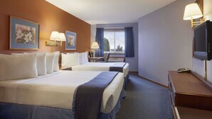 Ein Hotelzimmer mit zwei Betten, einem Schreibtisch, einem Stuhl, einem Fernseher und einem Fenster mit Vorhängen.