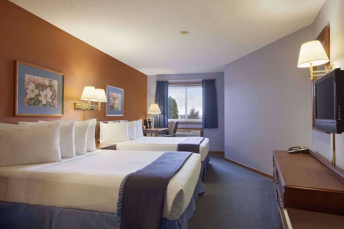 A hotel room with two beds, a desk, a chair, a television, and a window with curtains.