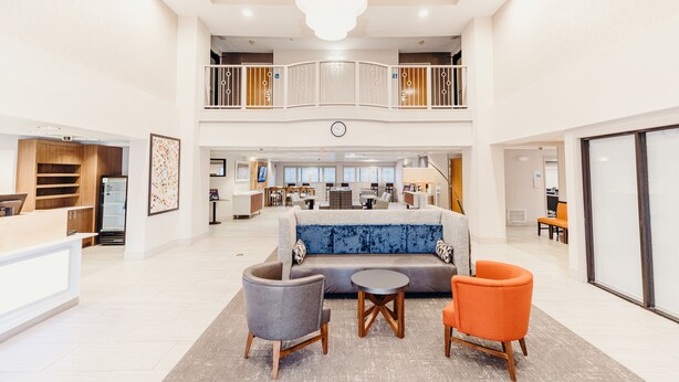 A spacious lobby with a high ceiling, a central seating area with a sofa and chairs, a reception desk, and a staircase leading to an upper level. - Holiday Inn Express Atlanta NE I-85 Clairmont by IHG (Atlanta)