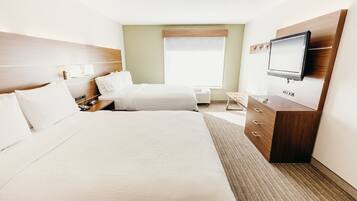 A hotel room with a large bed, a smaller bed, a TV mounted on the wall, a desk, and a window with blinds.