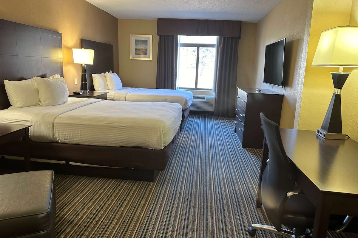 A hotel room with two beds, a desk, a chair, a TV, and a window with curtains.