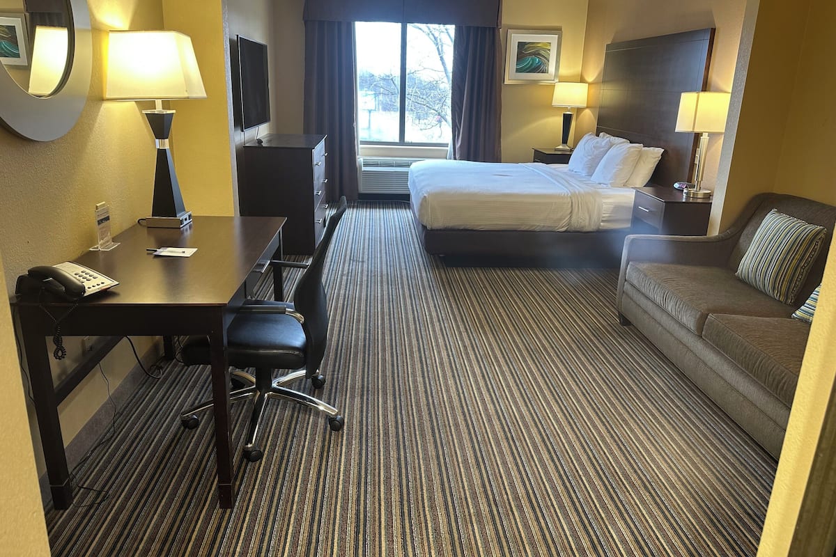 A hotel room with a bed, a desk with a telephone, a chair, a sofa, and two lamps.