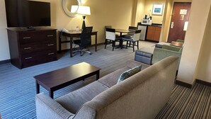 A hotel room with a sofa, a coffee table, a TV, a desk with a chair, and a kitchenette in the background.