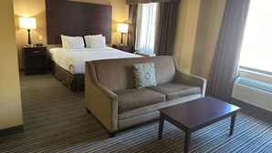 A hotel room with a large bed, a sofa, a small table, and two bedside lamps.