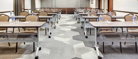 Une salle de conférence dotée de plusieurs tables et chaises, ainsi que de bouteilles d’eau et de verres.