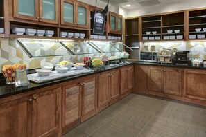 A buffet area with wooden cabinets, a glass display case, and a tiled backsplash. - Hyatt Place Boise/Towne Square (Boise)