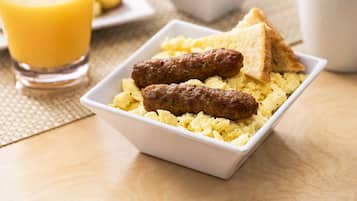 A breakfast setting with scrambled eggs, sausages, toast, and a glass of orange juice.