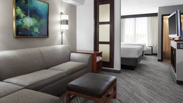 A hotel room with a sofa, a small table, a TV, a bed, and a painting on the wall.